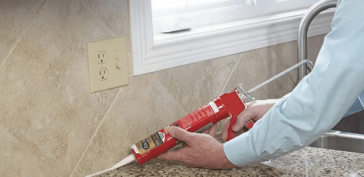 Handyman applying caulk along a kitchen backsplash and countertop seam in Sterling Heights, MI